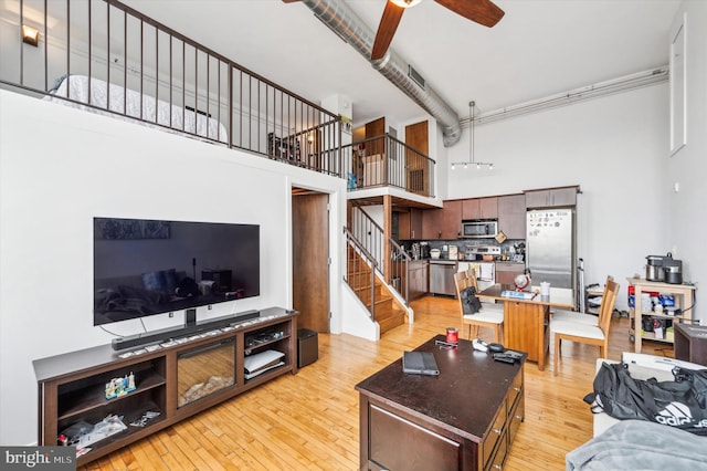 living room featuring ceiling fan, light hardwood / wood-style floors, and a high ceiling