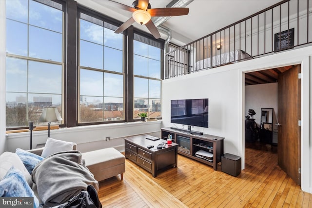 living room with ceiling fan, a towering ceiling, and light wood-type flooring