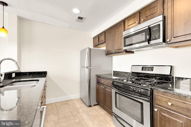 kitchen featuring sink, stainless steel appliances, dark stone countertops, pendant lighting, and light tile patterned floors