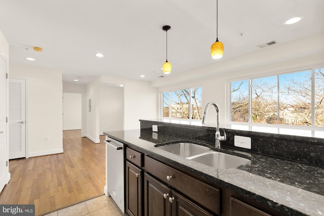 kitchen featuring dishwasher, sink, dark stone countertops, light wood-type flooring, and decorative light fixtures