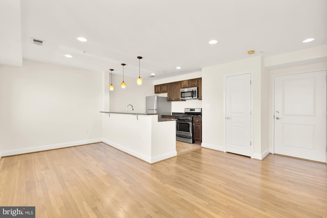 kitchen featuring kitchen peninsula, pendant lighting, a breakfast bar, appliances with stainless steel finishes, and light wood-type flooring