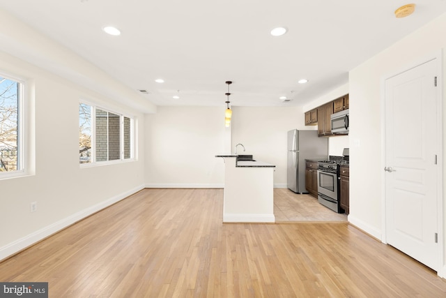 kitchen with hanging light fixtures, stainless steel appliances, a center island with sink, and light wood-type flooring