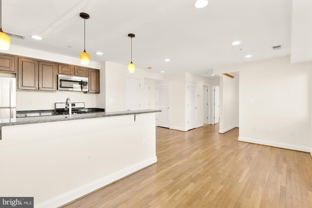 kitchen featuring dark stone counters, decorative light fixtures, light hardwood / wood-style floors, and white appliances