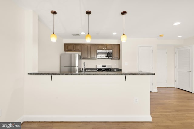 kitchen featuring kitchen peninsula, stainless steel appliances, sink, decorative light fixtures, and light hardwood / wood-style floors