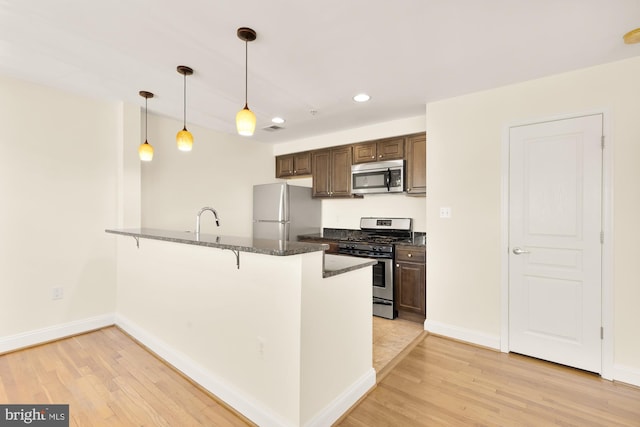 kitchen with pendant lighting, light hardwood / wood-style floors, a kitchen bar, kitchen peninsula, and stainless steel appliances