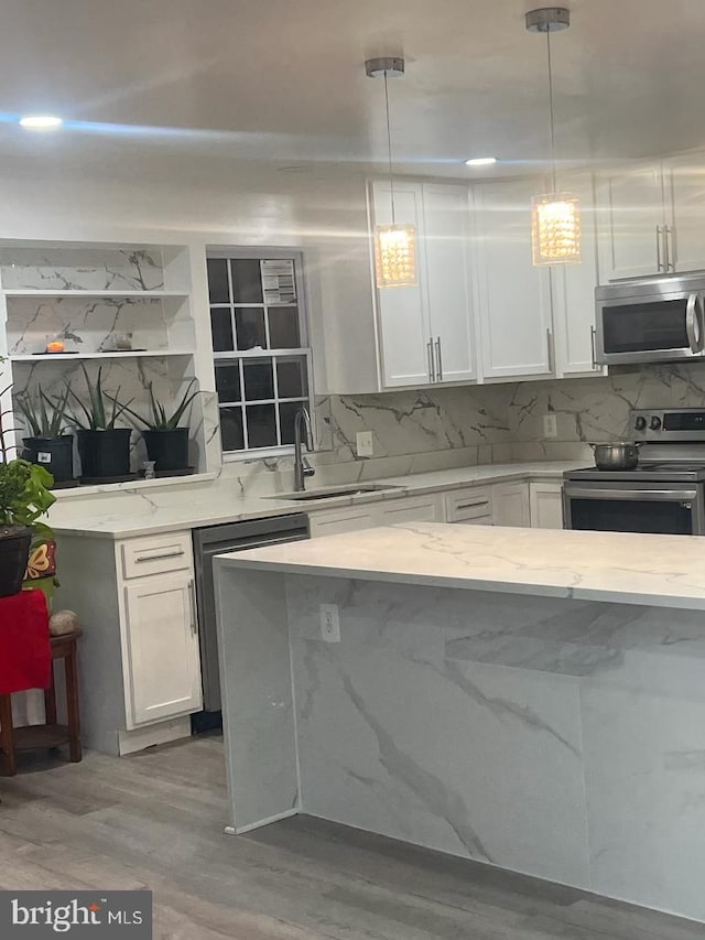 kitchen featuring light stone countertops, white cabinetry, stainless steel appliances, light hardwood / wood-style flooring, and pendant lighting