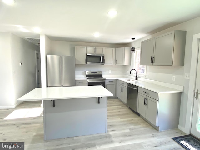 kitchen featuring gray cabinetry, a center island, pendant lighting, light hardwood / wood-style floors, and appliances with stainless steel finishes