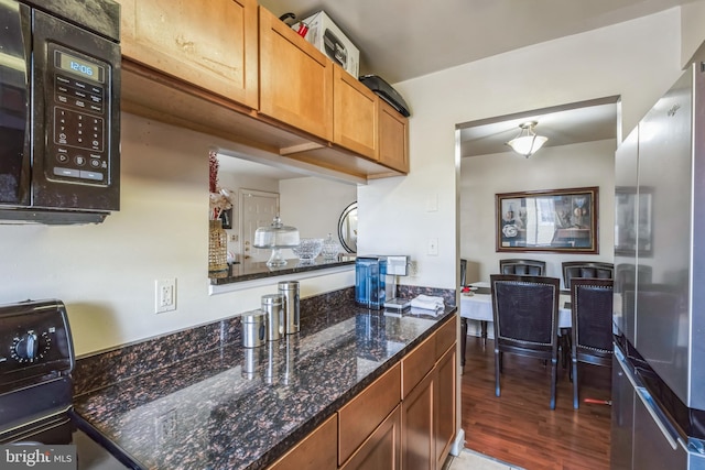 kitchen featuring wood-type flooring, stainless steel refrigerator, dark stone counters, and range