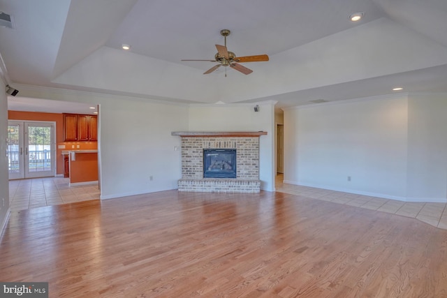 unfurnished living room featuring a brick fireplace, ceiling fan, french doors, and light hardwood / wood-style flooring