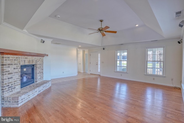 unfurnished living room with light wood-type flooring, ornamental molding, a tray ceiling, ceiling fan, and a fireplace