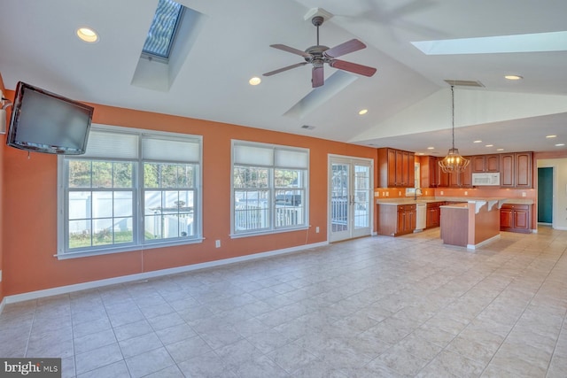 unfurnished living room featuring a skylight, light tile patterned floors, a healthy amount of sunlight, and ceiling fan with notable chandelier