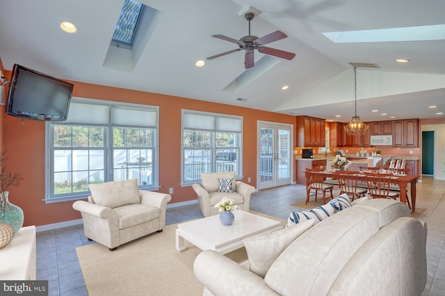 living room featuring light tile patterned floors, ceiling fan with notable chandelier, and lofted ceiling with skylight