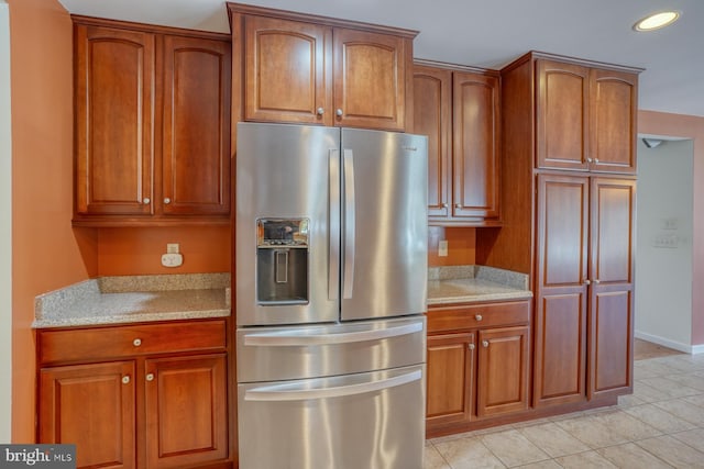 kitchen with stainless steel fridge, light tile patterned flooring, and light stone countertops