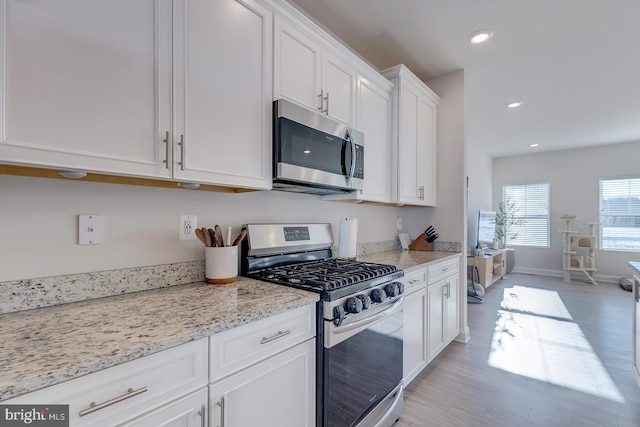 kitchen featuring light stone counters, light wood-type flooring, white cabinetry, and appliances with stainless steel finishes