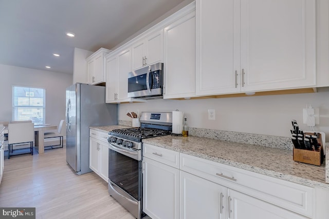 kitchen with light stone countertops, white cabinets, stainless steel appliances, and light wood-type flooring