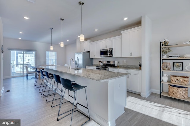 kitchen with decorative light fixtures, white cabinetry, stainless steel appliances, and an island with sink