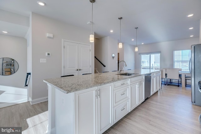 kitchen featuring appliances with stainless steel finishes, decorative light fixtures, white cabinetry, light stone countertops, and a center island with sink