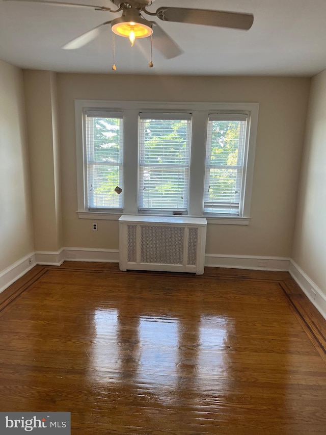 empty room with wood-type flooring, radiator heating unit, ceiling fan, and plenty of natural light