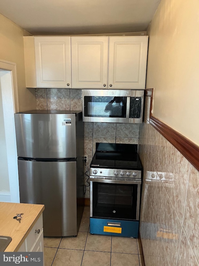 kitchen with tile walls, white cabinetry, light tile patterned floors, and appliances with stainless steel finishes