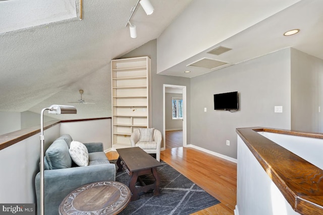 living area featuring lofted ceiling, attic access, a textured ceiling, wood finished floors, and baseboards