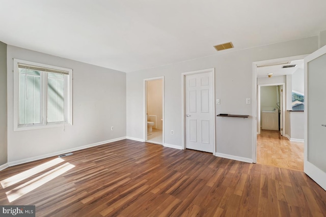 unfurnished bedroom featuring visible vents, ensuite bath, baseboards, and wood finished floors