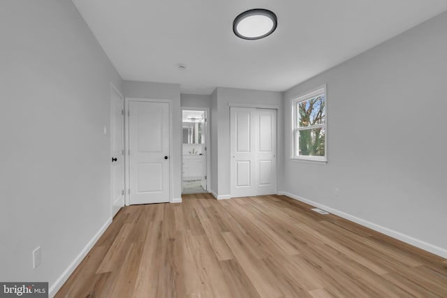 unfurnished bedroom with connected bathroom, a closet, and light hardwood / wood-style flooring