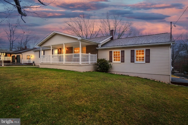 back house at dusk featuring a lawn and covered porch