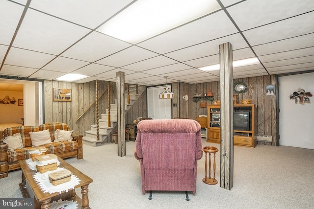 carpeted living room with a paneled ceiling and wood walls