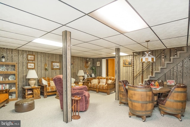 living room featuring a paneled ceiling, wood walls, and carpet