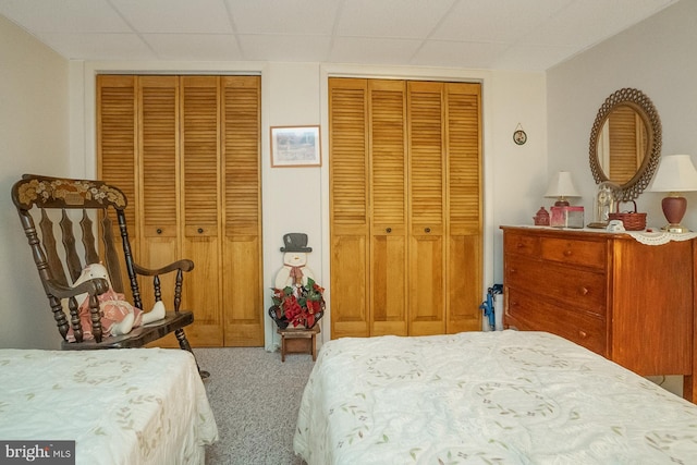 bedroom with light carpet, a drop ceiling, and multiple closets