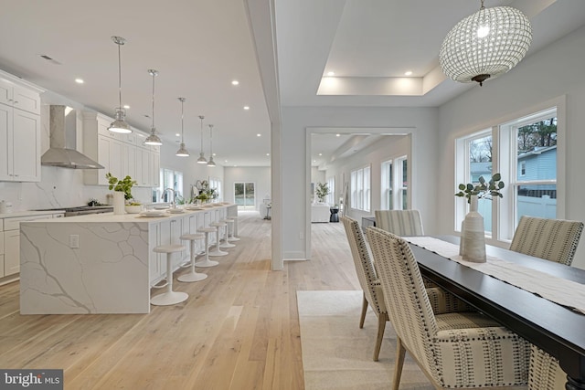 dining space with light wood-type flooring, a tray ceiling, and a wealth of natural light