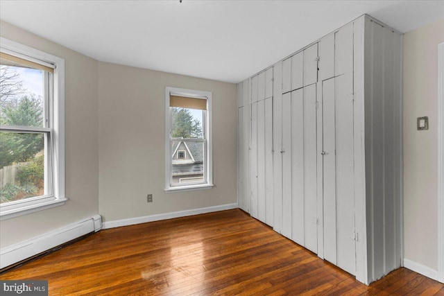 unfurnished bedroom featuring multiple windows, baseboard heating, and dark wood-type flooring