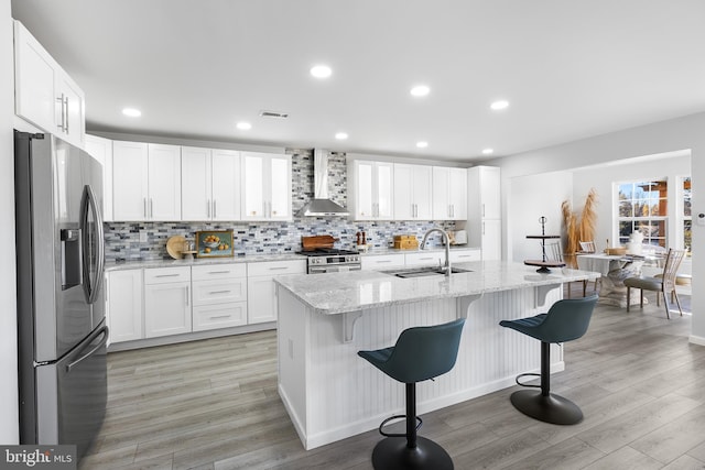 kitchen with wall chimney exhaust hood, stainless steel appliances, sink, light hardwood / wood-style floors, and white cabinetry