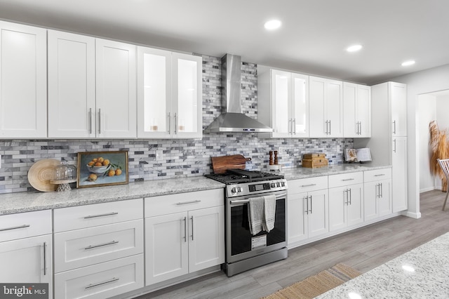 kitchen featuring wall chimney exhaust hood, white cabinetry, light wood-type flooring, and stainless steel range with gas cooktop