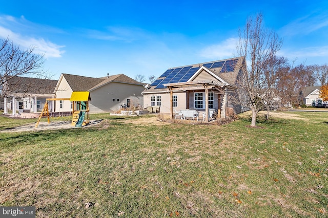 rear view of property featuring a playground, a patio area, a yard, and solar panels