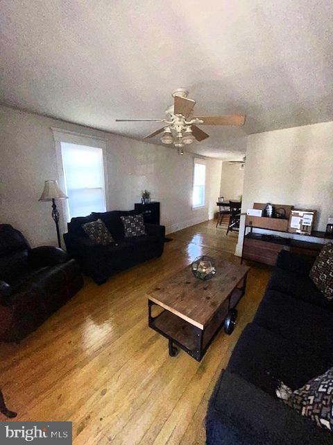 living room featuring wood-type flooring, a textured ceiling, and ceiling fan