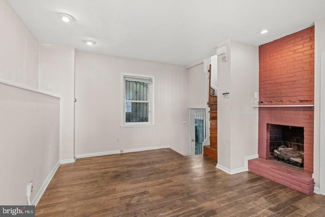 unfurnished living room featuring dark wood-type flooring and a brick fireplace