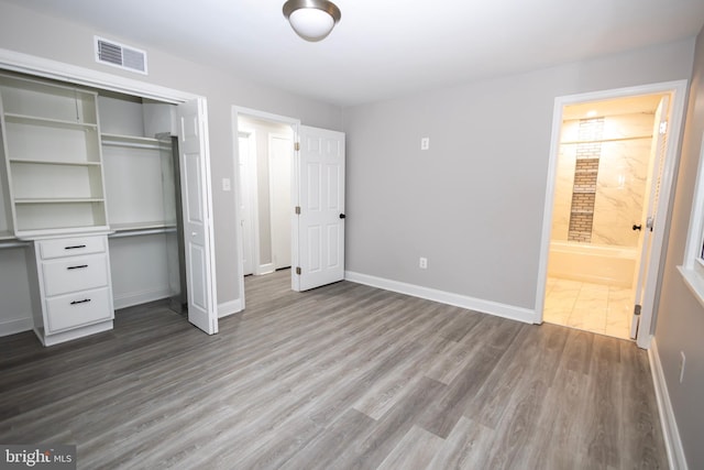 unfurnished bedroom featuring ensuite bathroom, wood-type flooring, and a closet