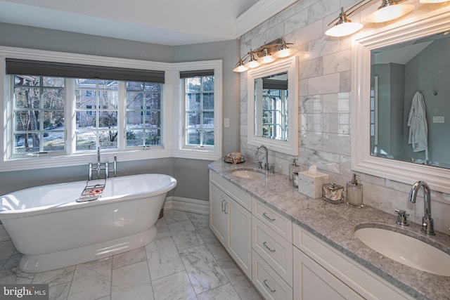 bathroom with double vanity, marble finish floor, a freestanding tub, and a sink