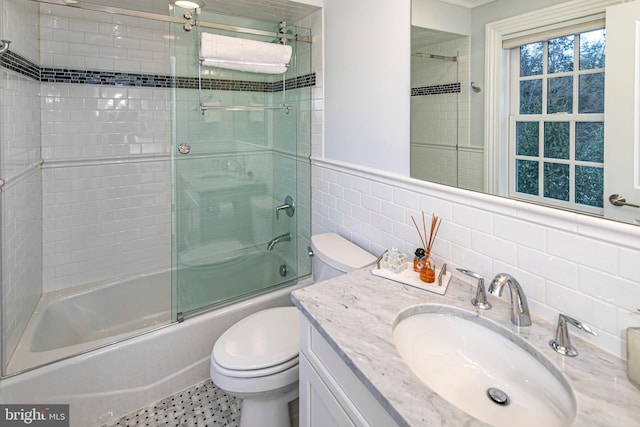 bathroom with wainscoting, toilet, combined bath / shower with glass door, vanity, and tile walls