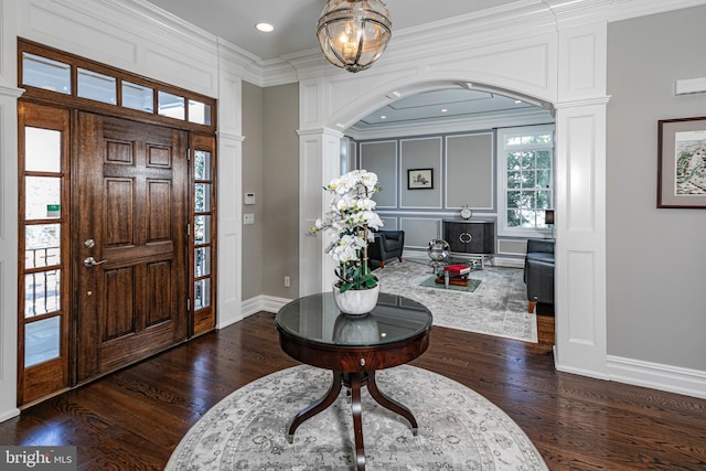 foyer featuring baseboards, a decorative wall, crown molding, and wood finished floors