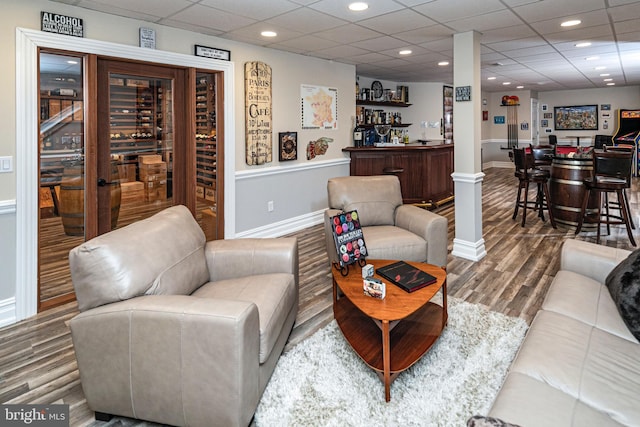 living room with baseboards, wood finished floors, a bar, ornate columns, and recessed lighting