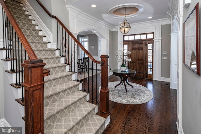 entrance foyer with arched walkways, crown molding, dark wood finished floors, ornate columns, and baseboards