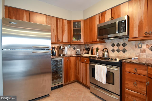 kitchen featuring tasteful backsplash, wine cooler, dark stone countertops, light tile patterned floors, and appliances with stainless steel finishes