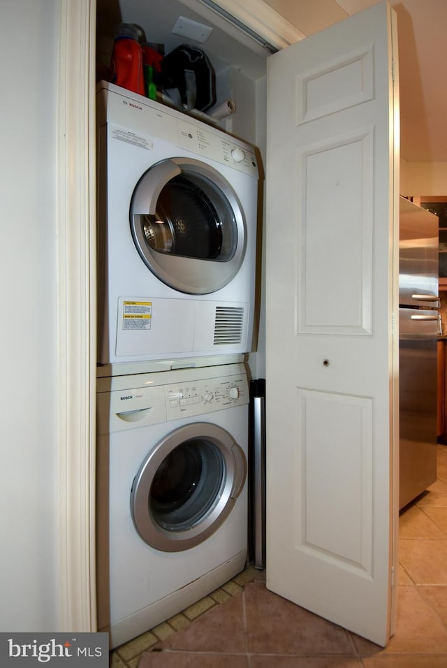 clothes washing area with light tile patterned floors and stacked washer / dryer