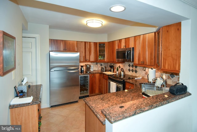 kitchen featuring kitchen peninsula, appliances with stainless steel finishes, tasteful backsplash, beverage cooler, and dark stone countertops