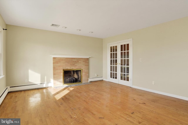 unfurnished living room featuring a brick fireplace, a baseboard heating unit, light hardwood / wood-style flooring, and french doors