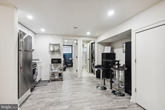 kitchen with white cabinets, light hardwood / wood-style flooring, stainless steel refrigerator, and stacked washing maching and dryer