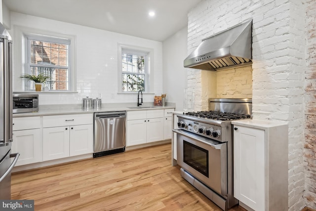 kitchen featuring white cabinetry, sink, wall chimney range hood, light hardwood / wood-style floors, and appliances with stainless steel finishes