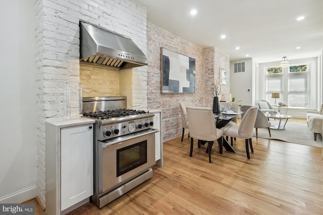 kitchen with wall chimney range hood, high end stainless steel range, and light hardwood / wood-style flooring